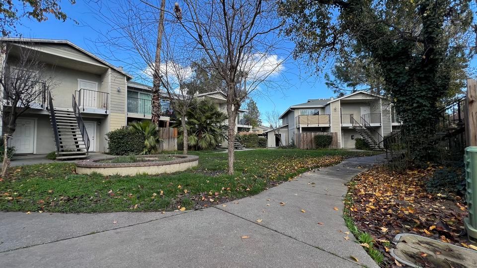 Suburban apartment walkway curving past trees and lawns on a clear blue day