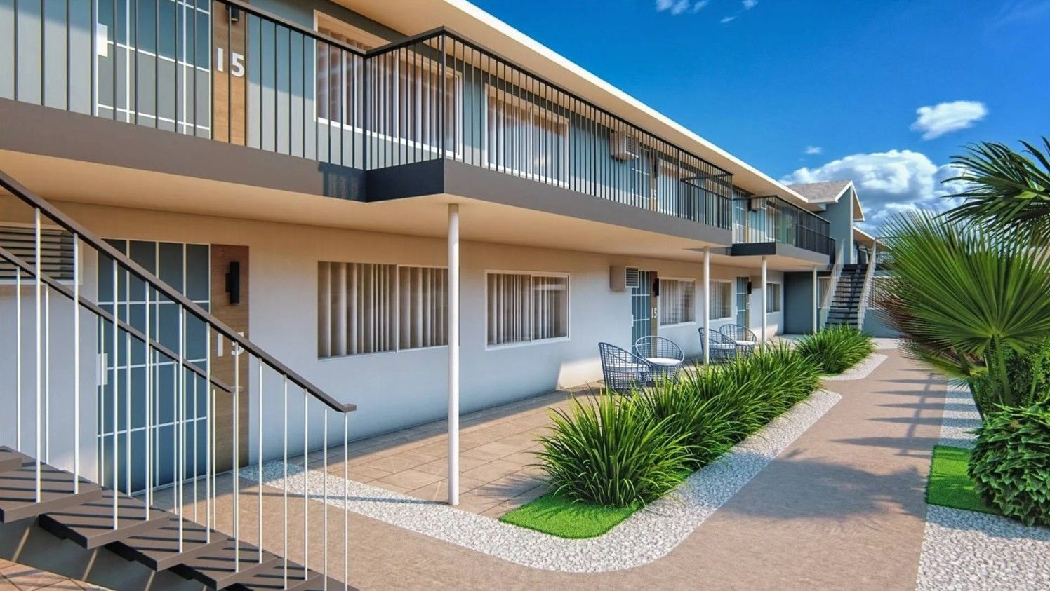 Exterior of a two-story motel with balcony walkways, stairs, and landscaped pathway in bright sunlight
