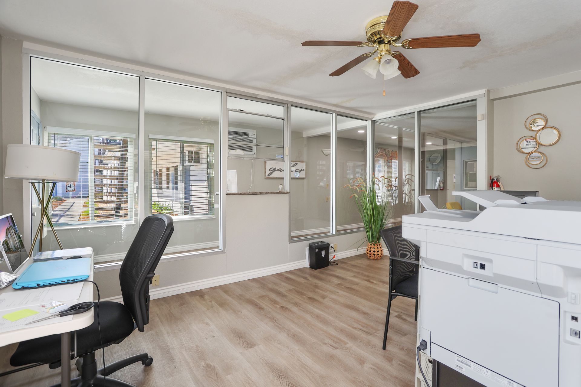 Bright home office with white printer, desk, black chair, and large windows overlooking a balcony.