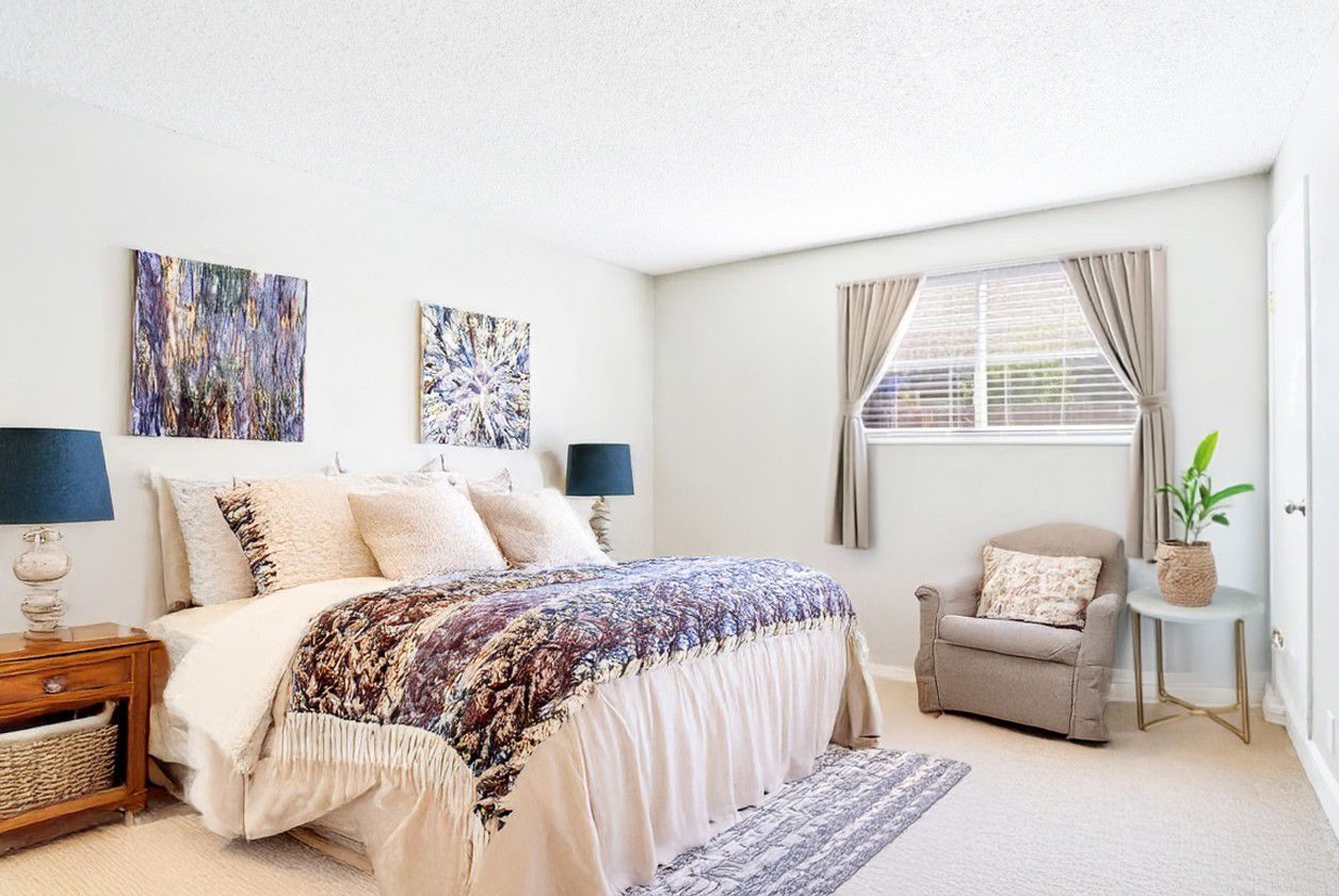 Bright bedroom with white bedding, purple accents, two wall art pieces, and a window seat chair.