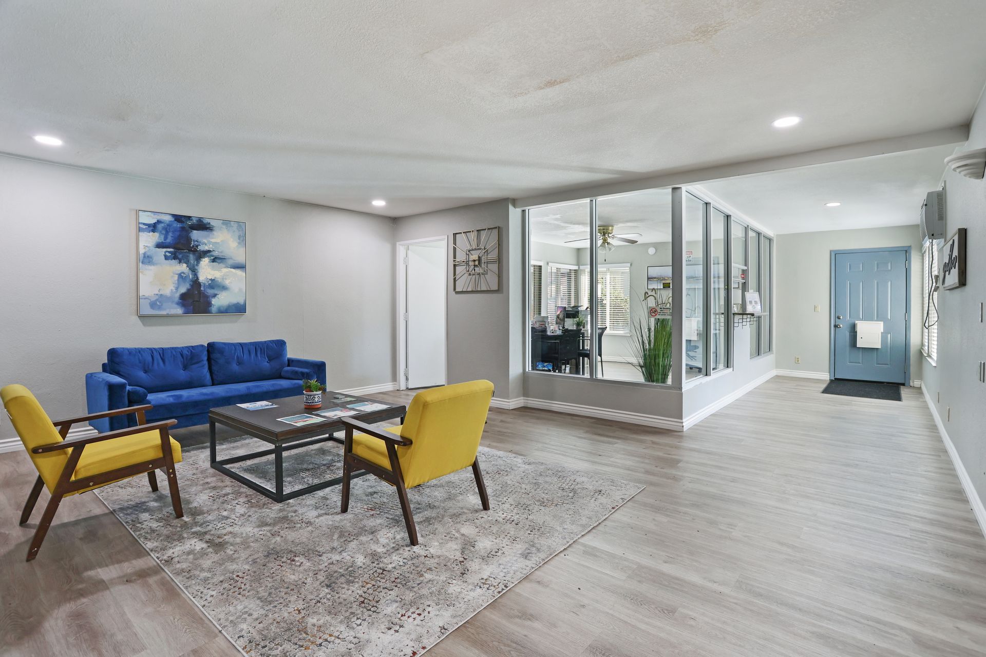 Bright living room with blue sofa, yellow chairs, glass walls, and a light gray rug