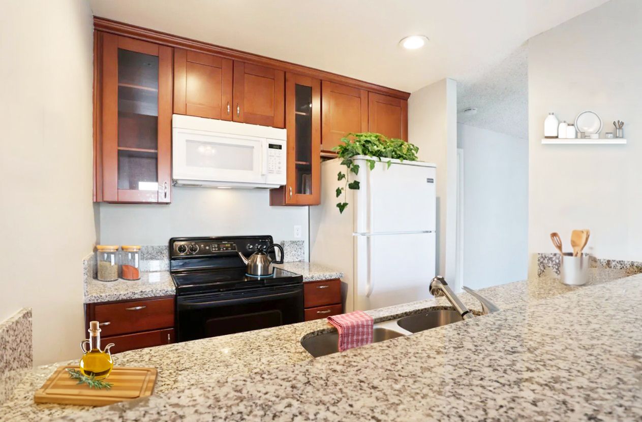 Modern kitchen with granite island, wood cabinets, black stove, white fridge, and a potted plant near the wall.