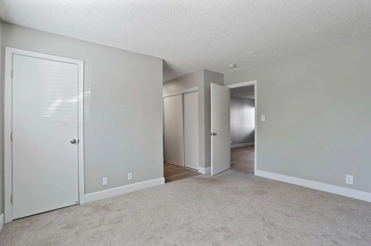 Empty beige bedroom with carpet, closed white closet door, and doorway to a hall