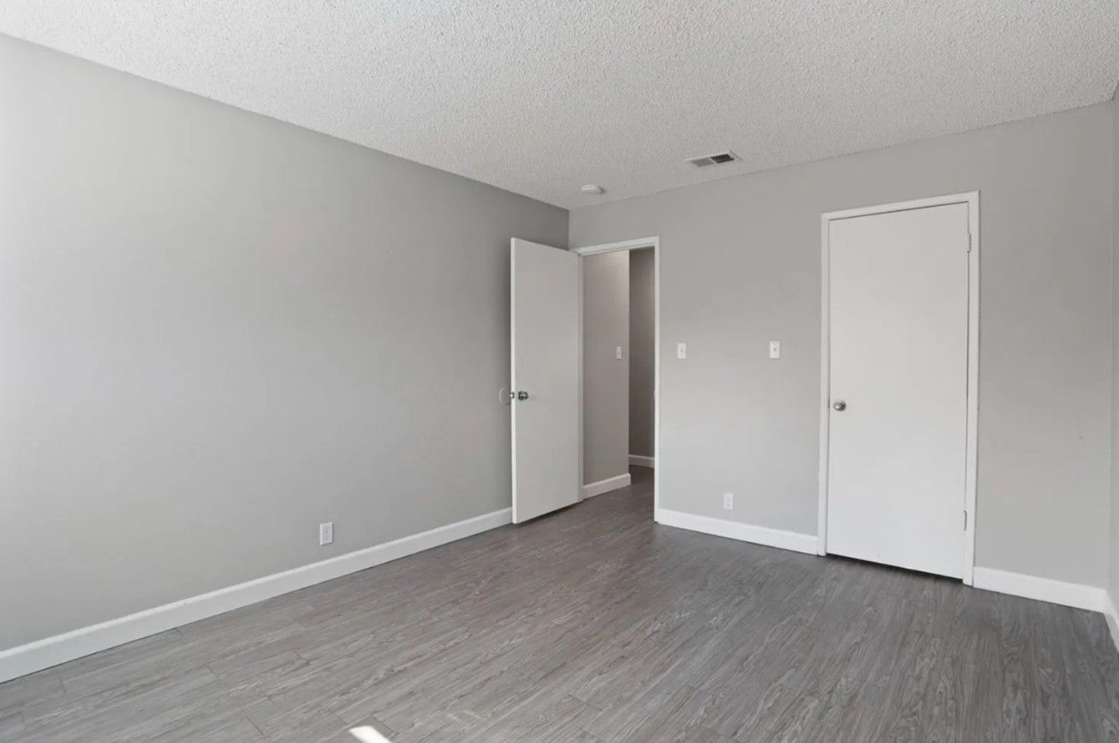 Empty gray bedroom with open door, white closet doors, and gray wood flooring