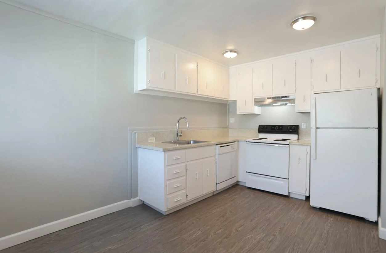 Bright white kitchen with cabinets, stove, refrigerator, and beige flooring