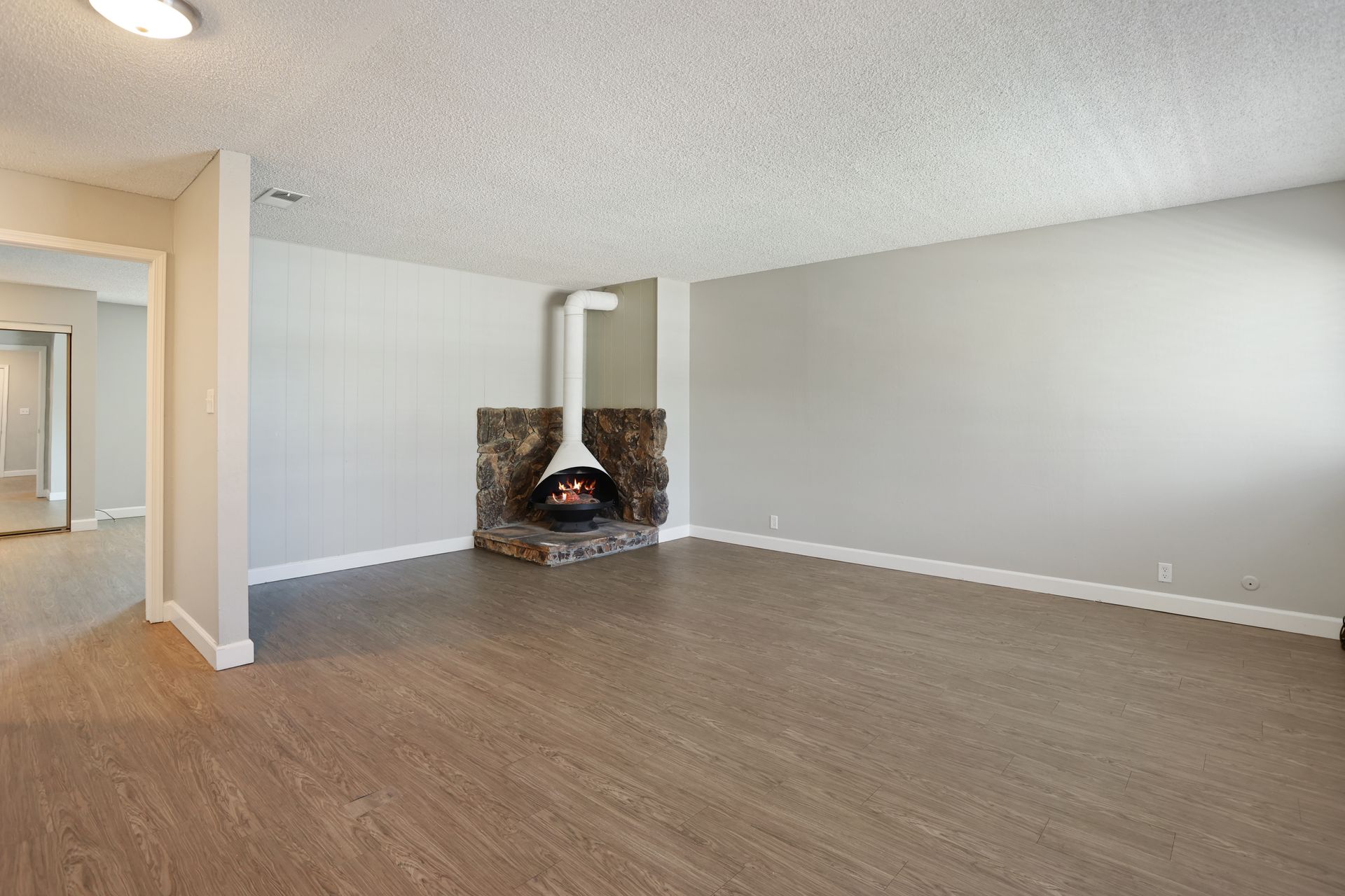 Empty living room with wood floor, light gray walls, and a corner fireplace.
