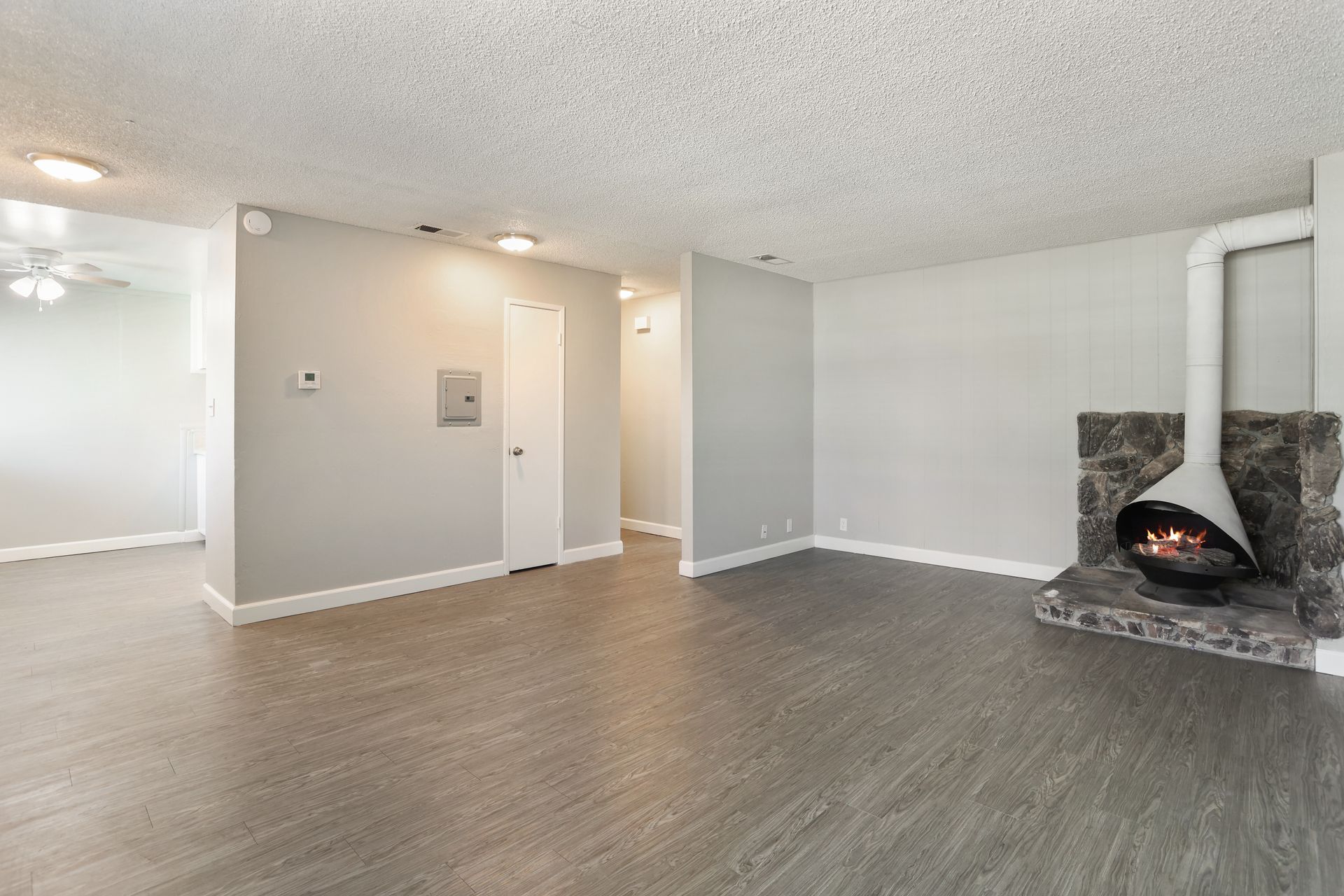 Empty living room with gray wood floors, white walls, recessed lights, and a corner fireplace