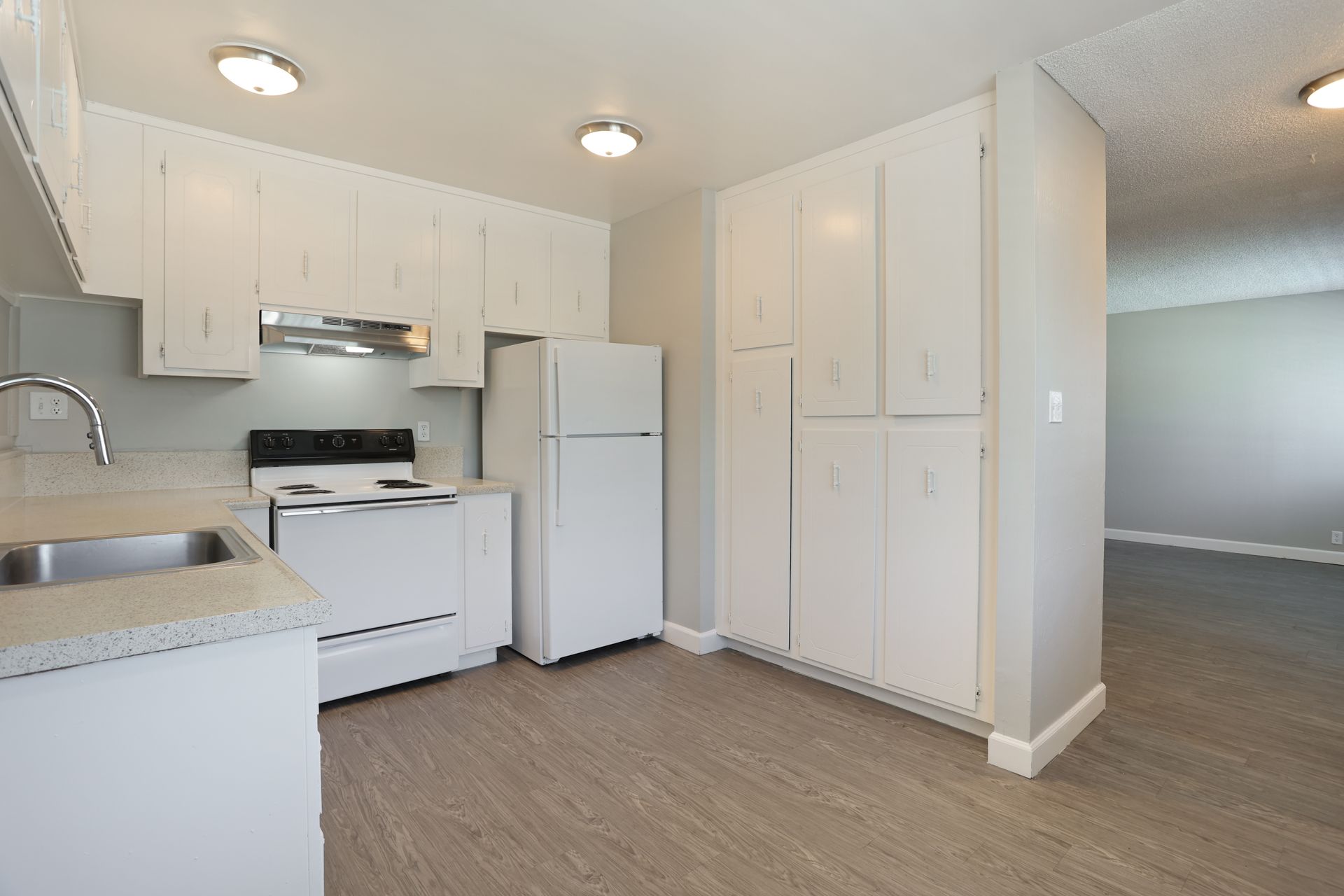 Bright white kitchen with stove, refrigerator, cabinets, and carpeted floor