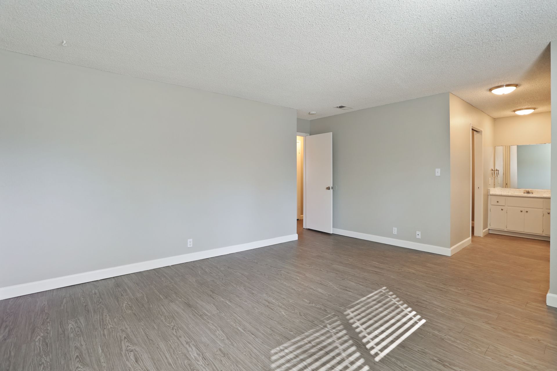 Empty living room with gray carpet, light walls, and a view into a kitchen area.