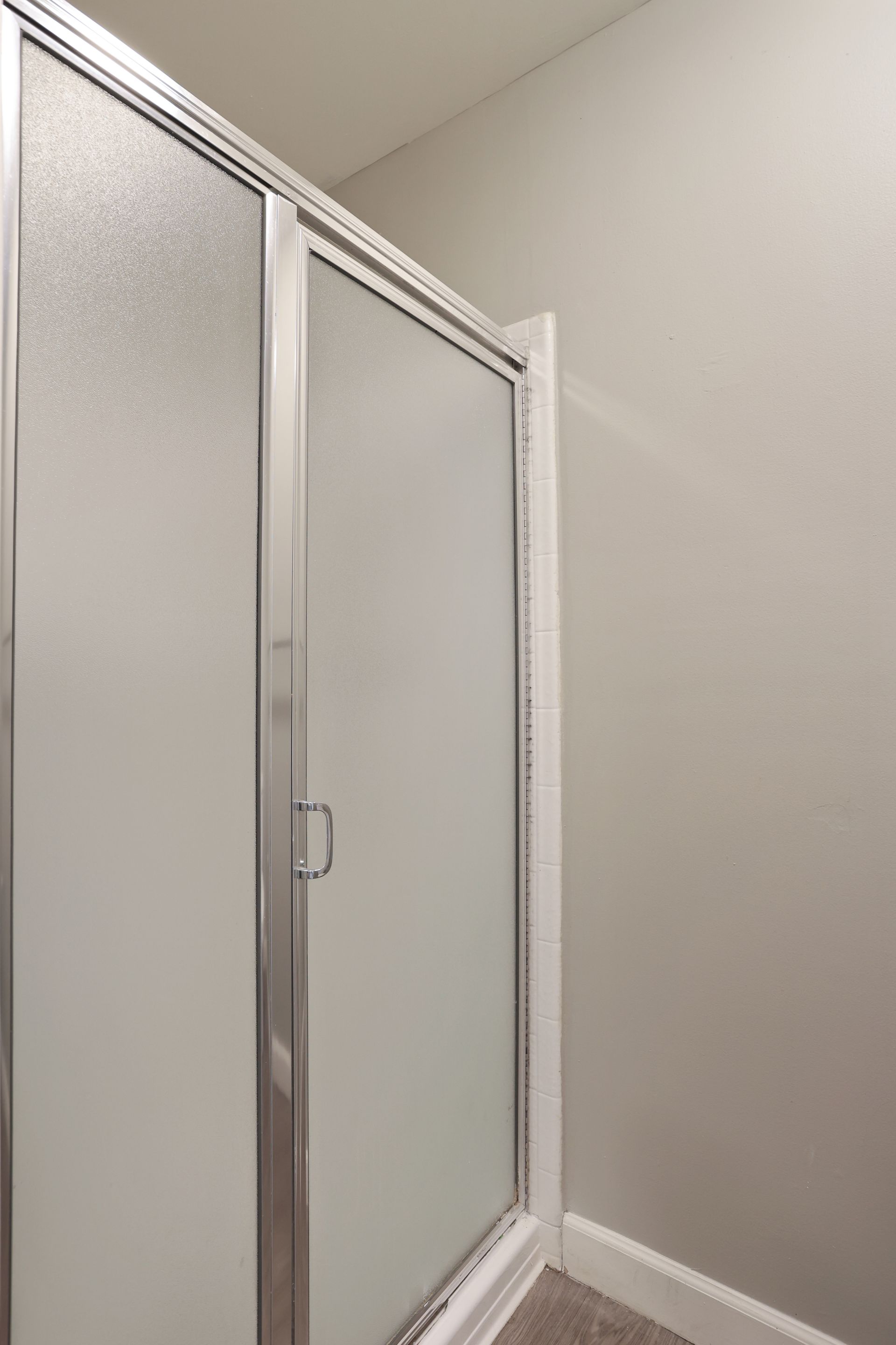 Glass shower door in a small bathroom with white walls and trim