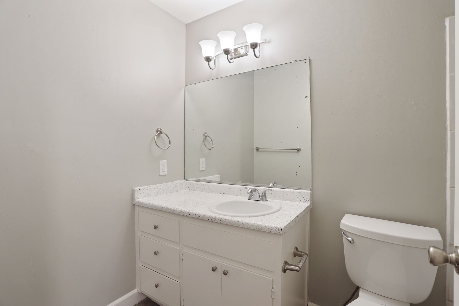 Small bathroom with white vanity, large mirror, three-light fixture, and toilet.