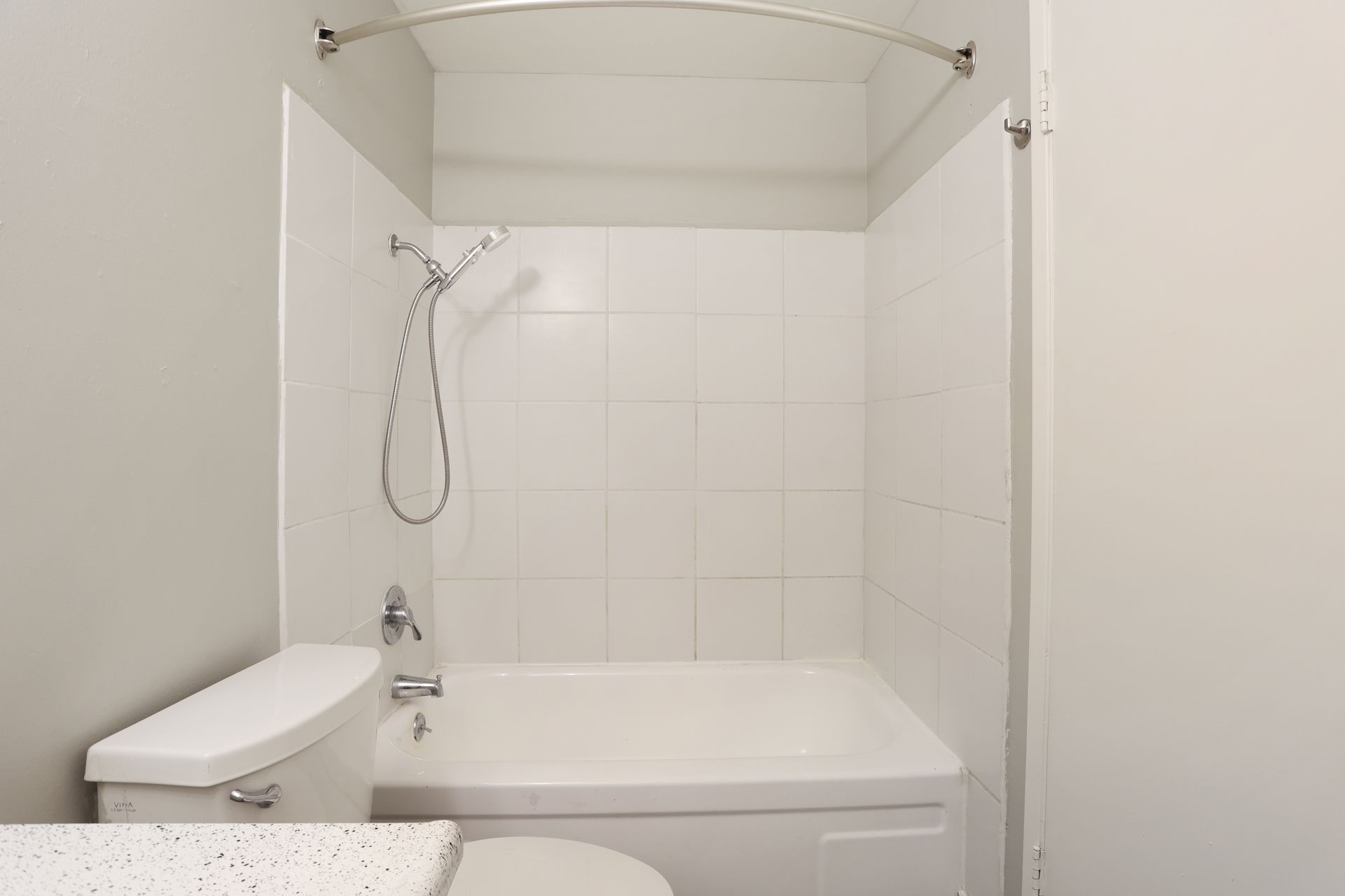 Small white bathroom with toilet, bathtub, and shower wand behind a clear curtain rod.
