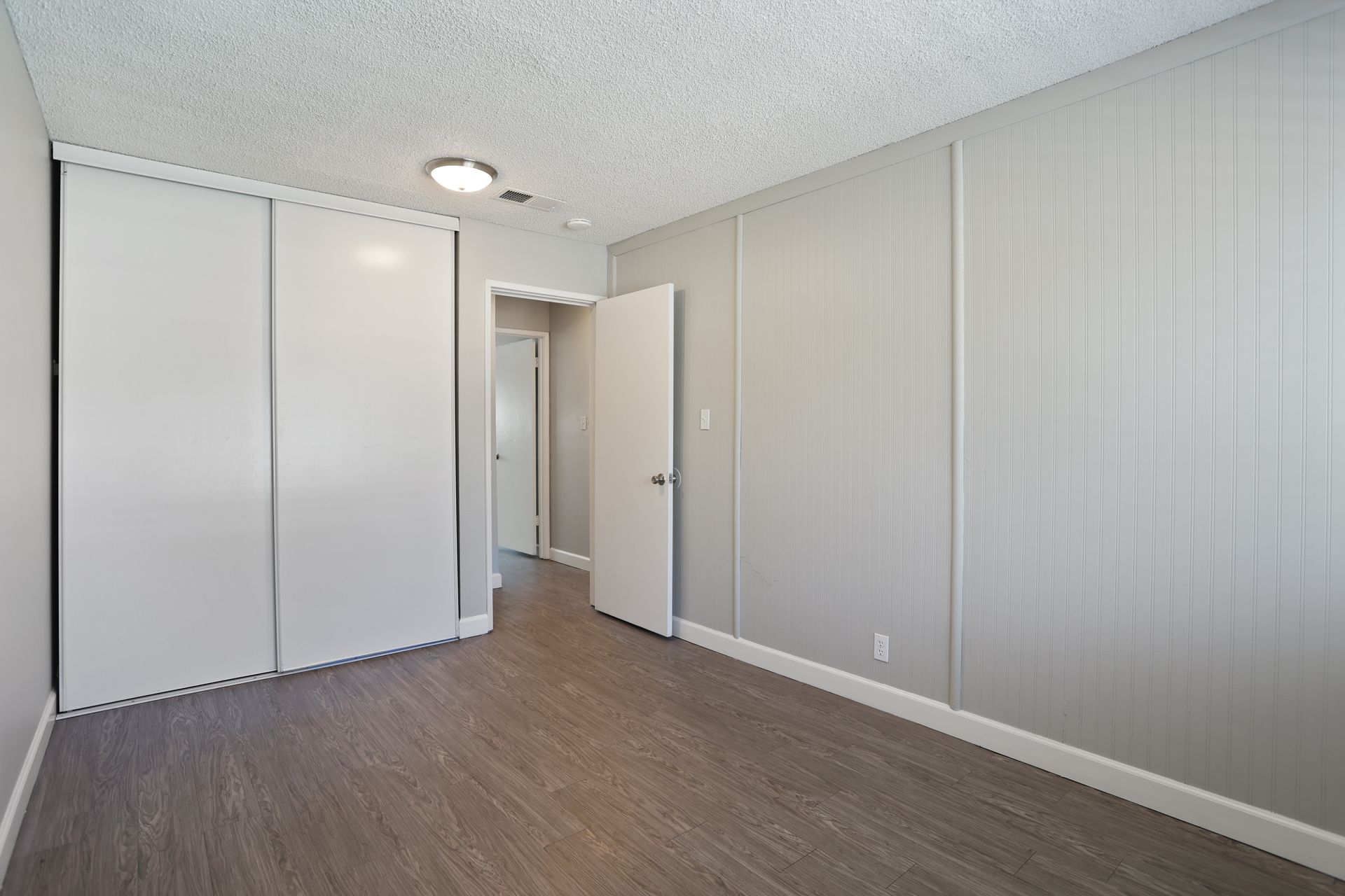 Empty bedroom with white walls, closet doors, and gray wood flooring.