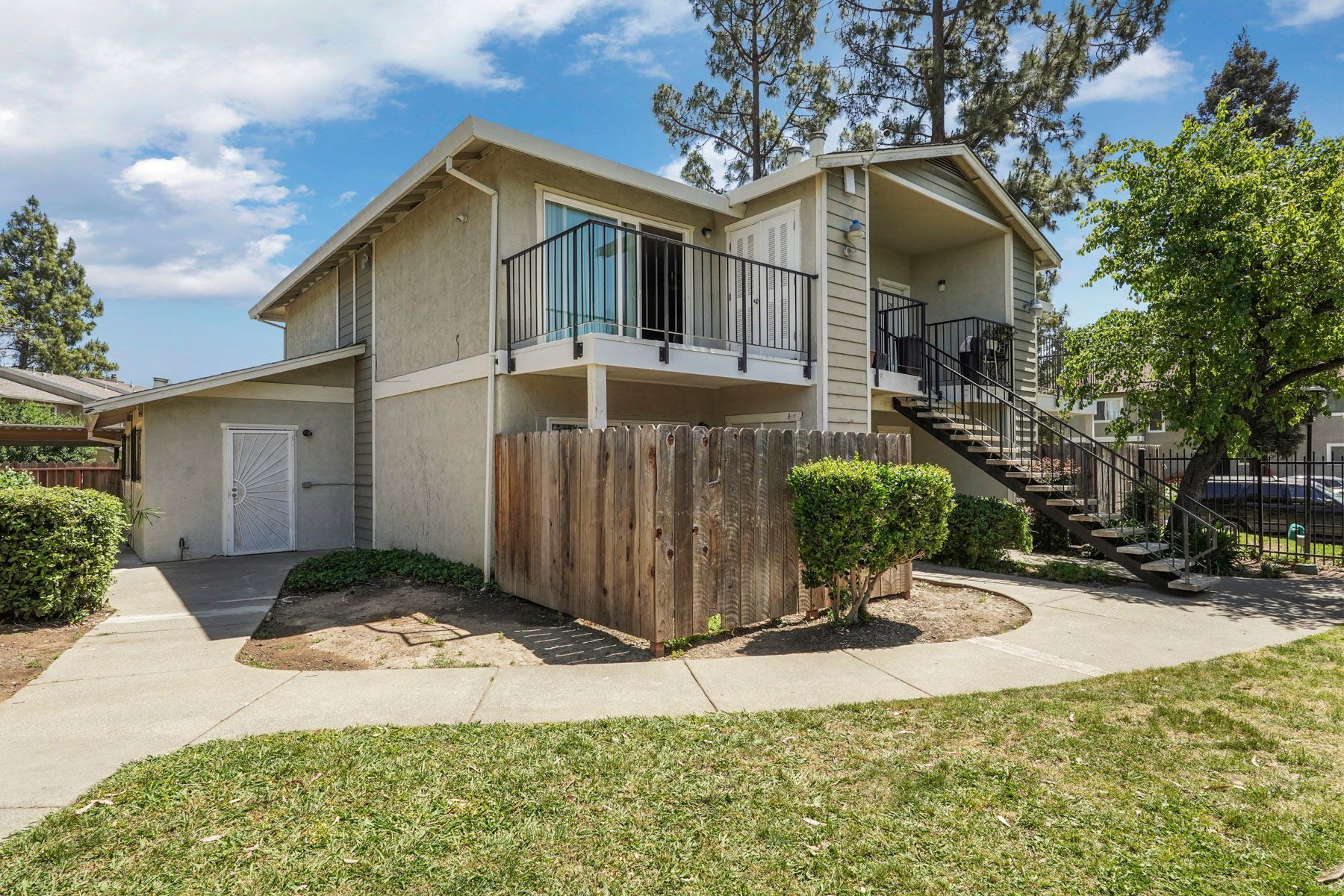 Suburban house with beige siding, front porch, garage, and a fenced yard on a sunny day