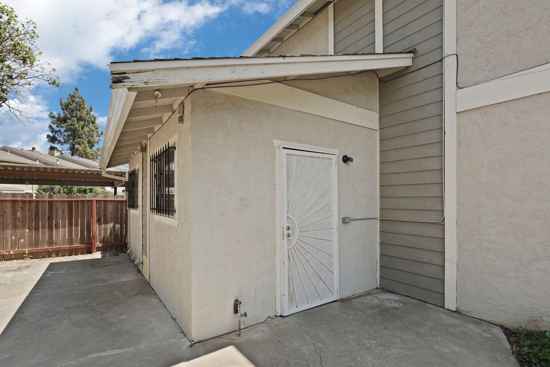 Exterior side entrance with a white door and concrete walkway beside a beige building
