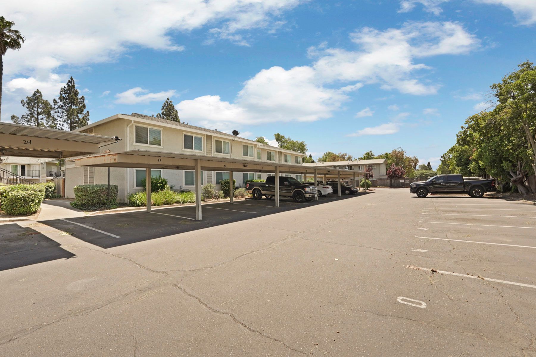 Covered parking lot beside a beige apartment complex under a bright blue sky