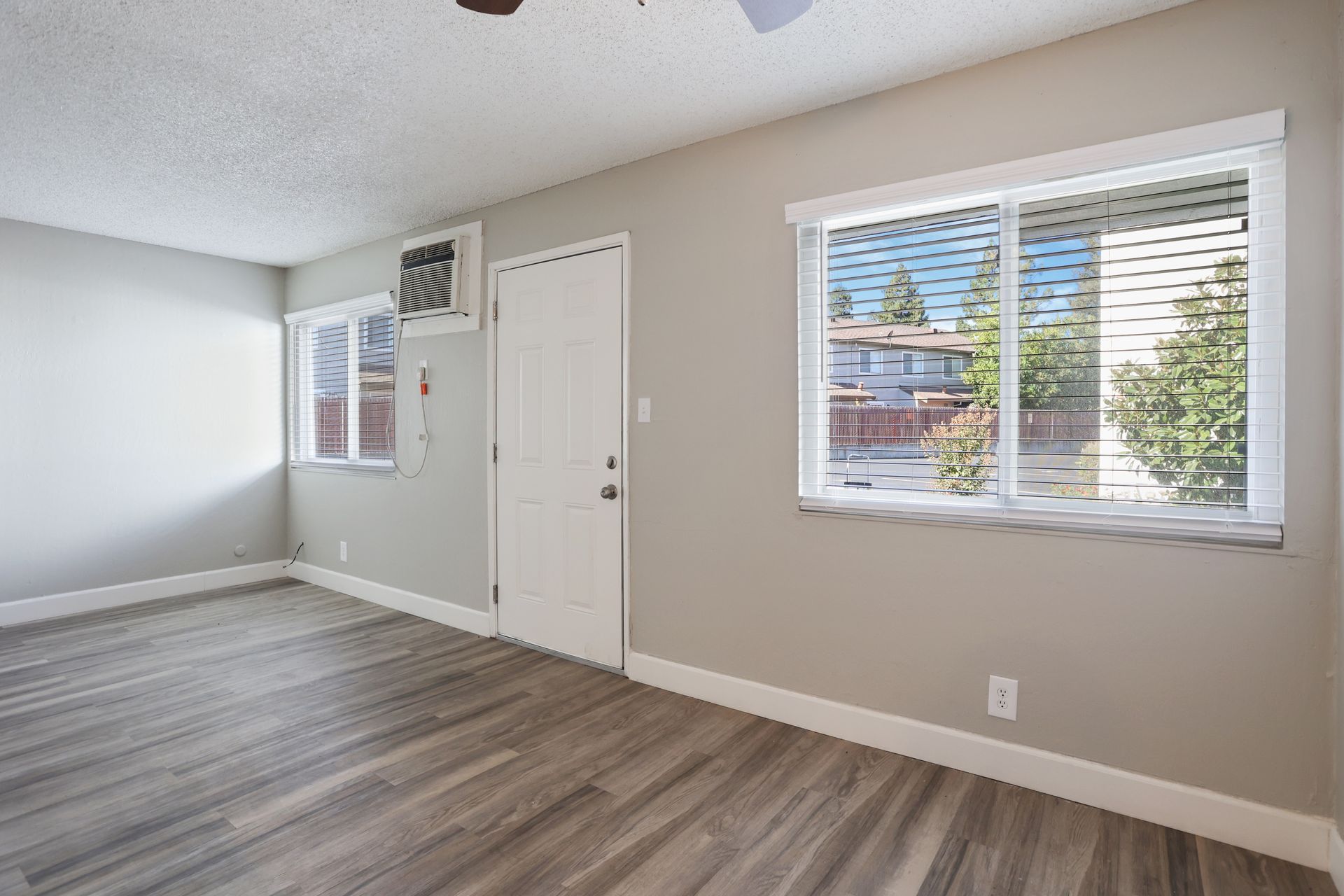 Empty bedroom with gray wood flooring, white walls, and two windows letting in daylight.
