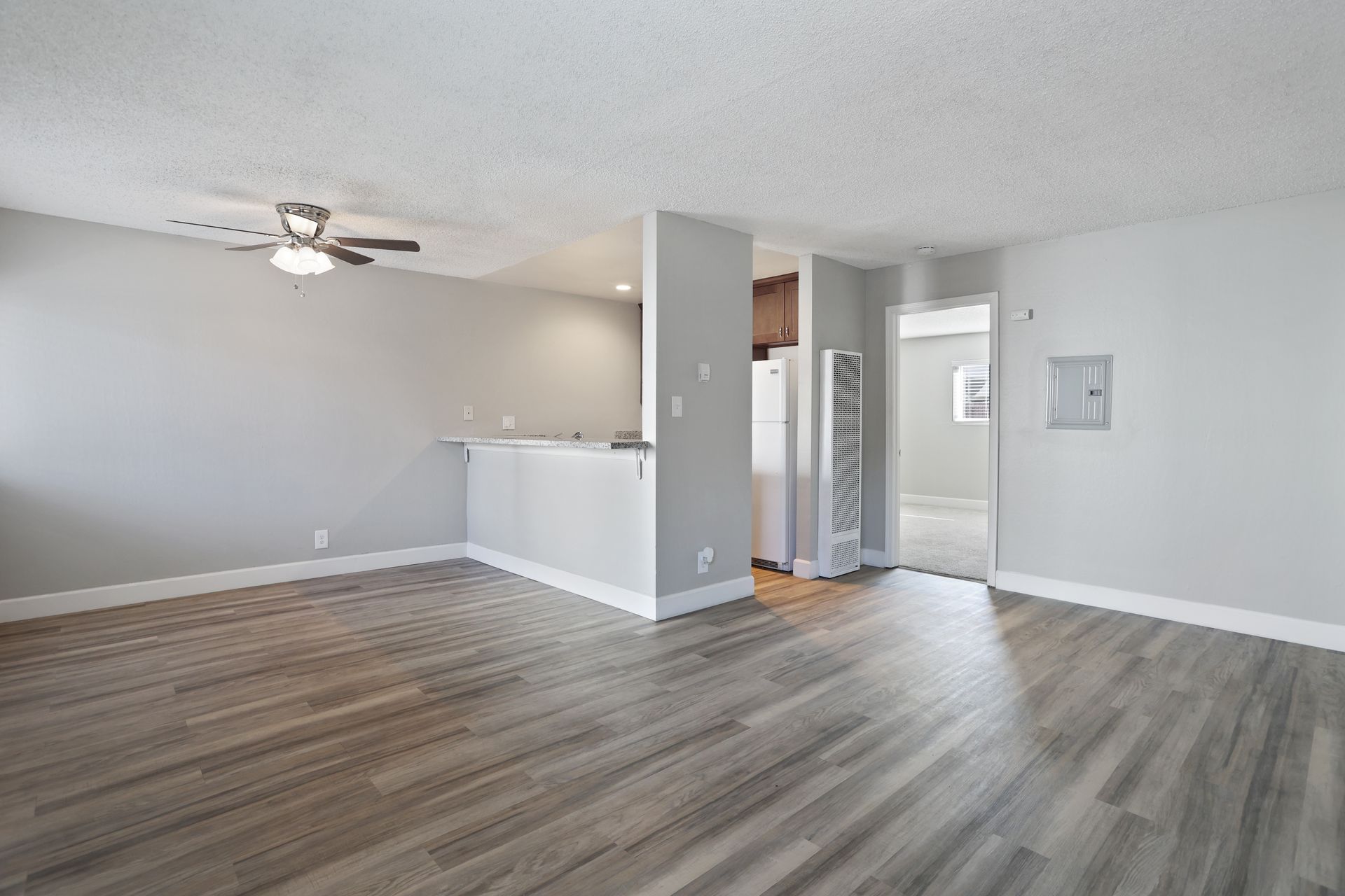Empty modern living room with gray walls, wood-look floor, ceiling fan, and open entryway