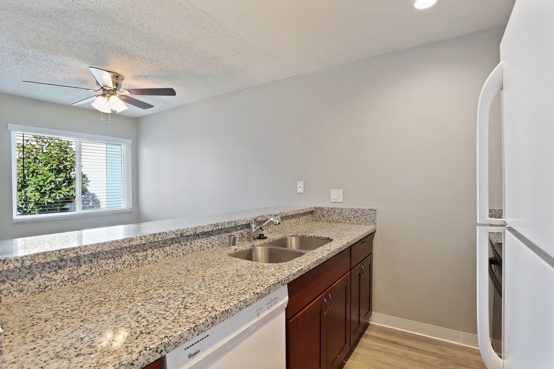 Kitchen with speckled granite counter, double sink, white cabinets, and a window by the dining area