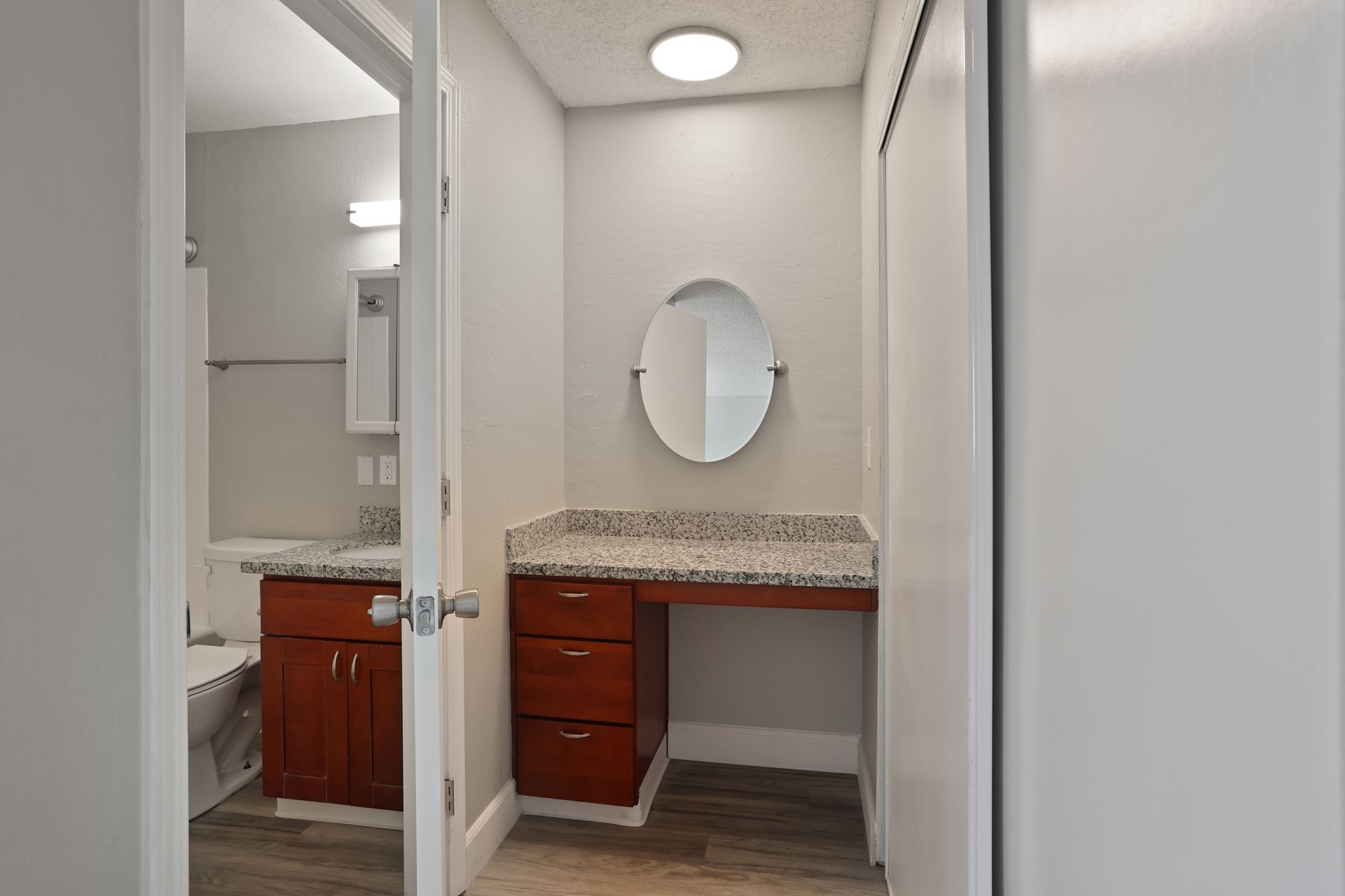 Bathroom vanity with granite countertop, oval mirror, and open doorway in a white interior.