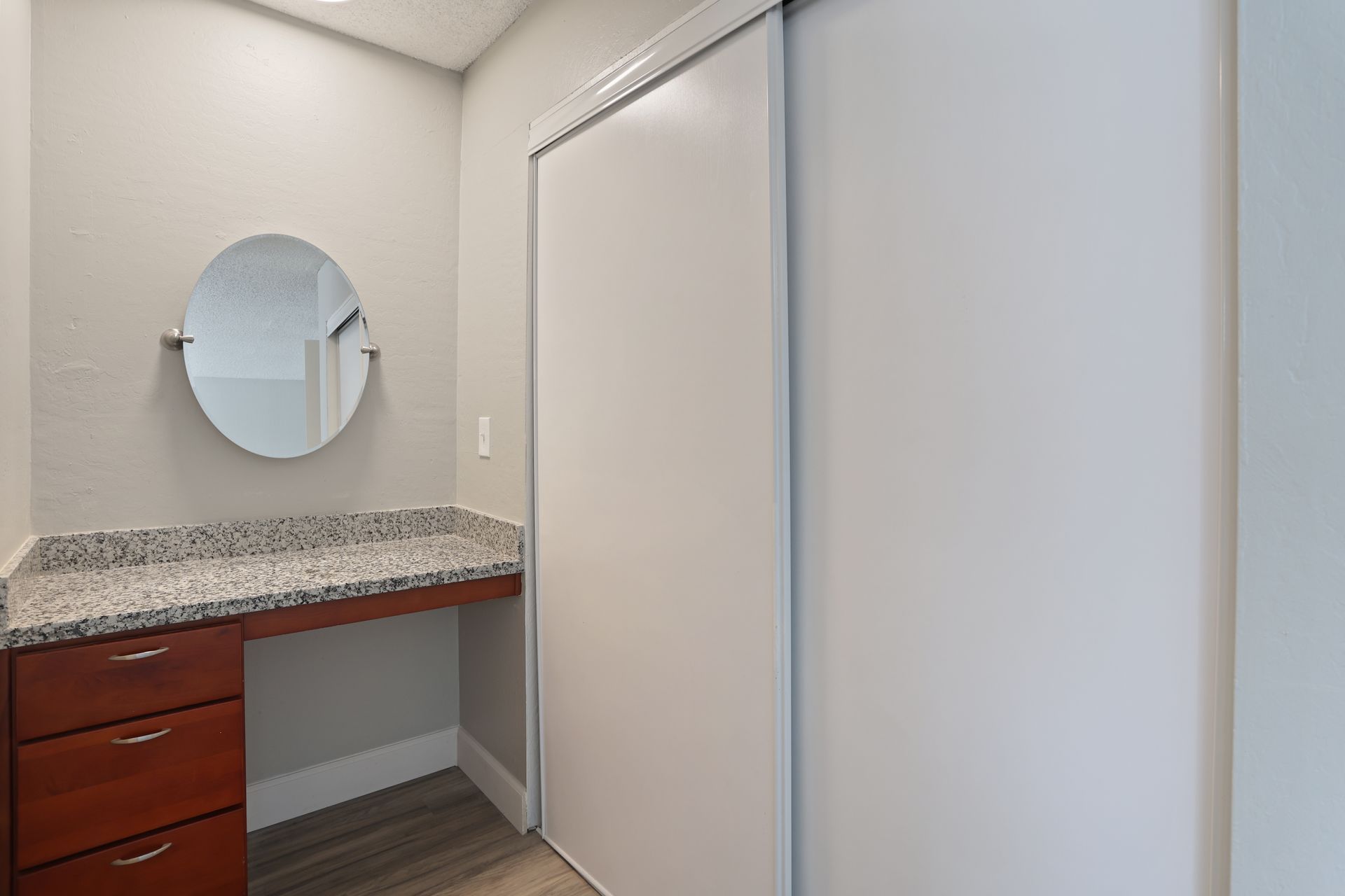 Small dressing area with a granite countertop, round mirror, and sliding closet doors.