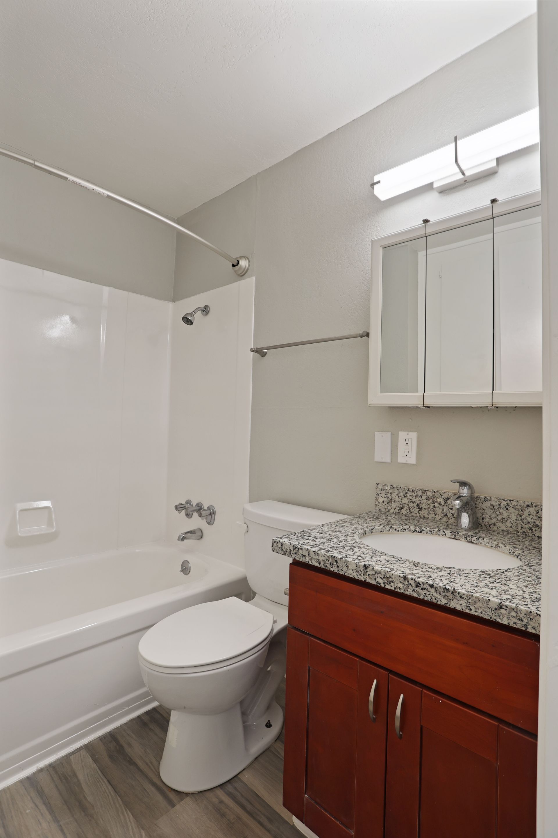 Small bathroom with a shower-tub, toilet, granite vanity, and mirrored cabinet.