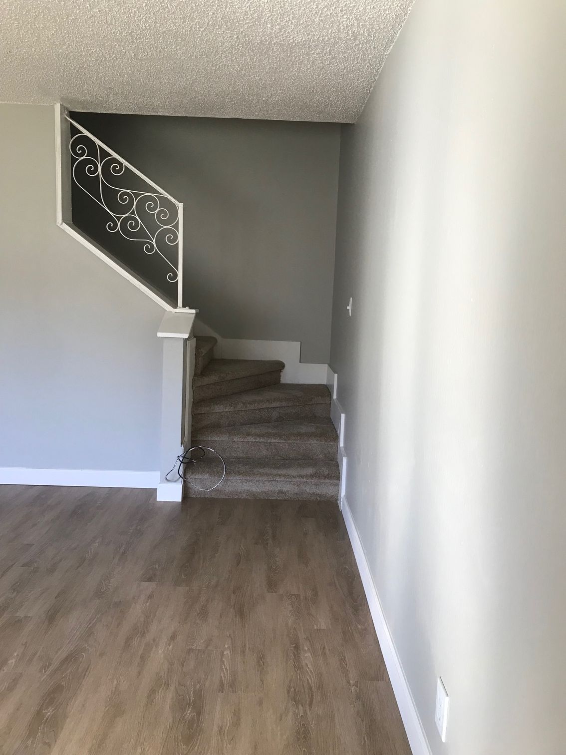 Empty hallway with carpeted stairs, white walls, and wood flooring leading to an upper landing