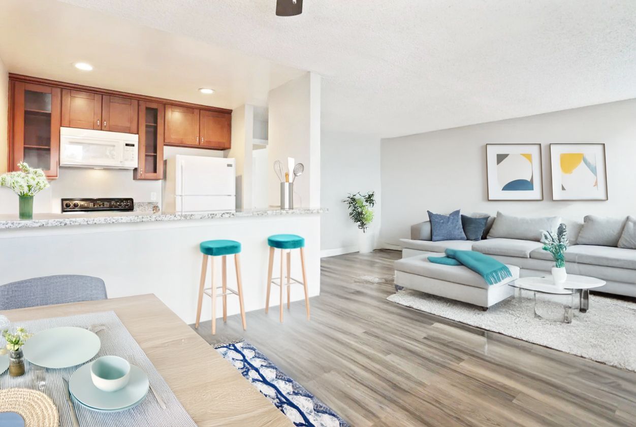 Bright open-plan kitchen and living room with white sofa, wood floors, and teal stools at the island.