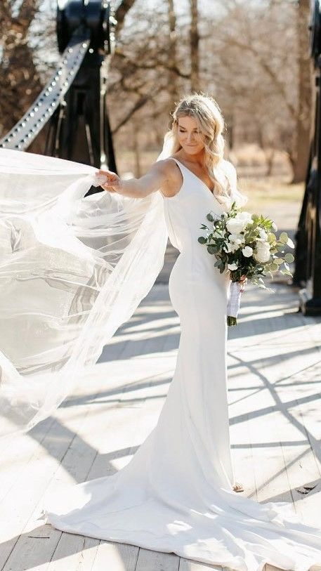 A bride in a white dress is holding a bouquet of flowers and her veil is blowing in the wind.