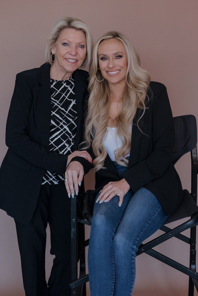 Two women are posing for a picture while sitting on makeup chairs.