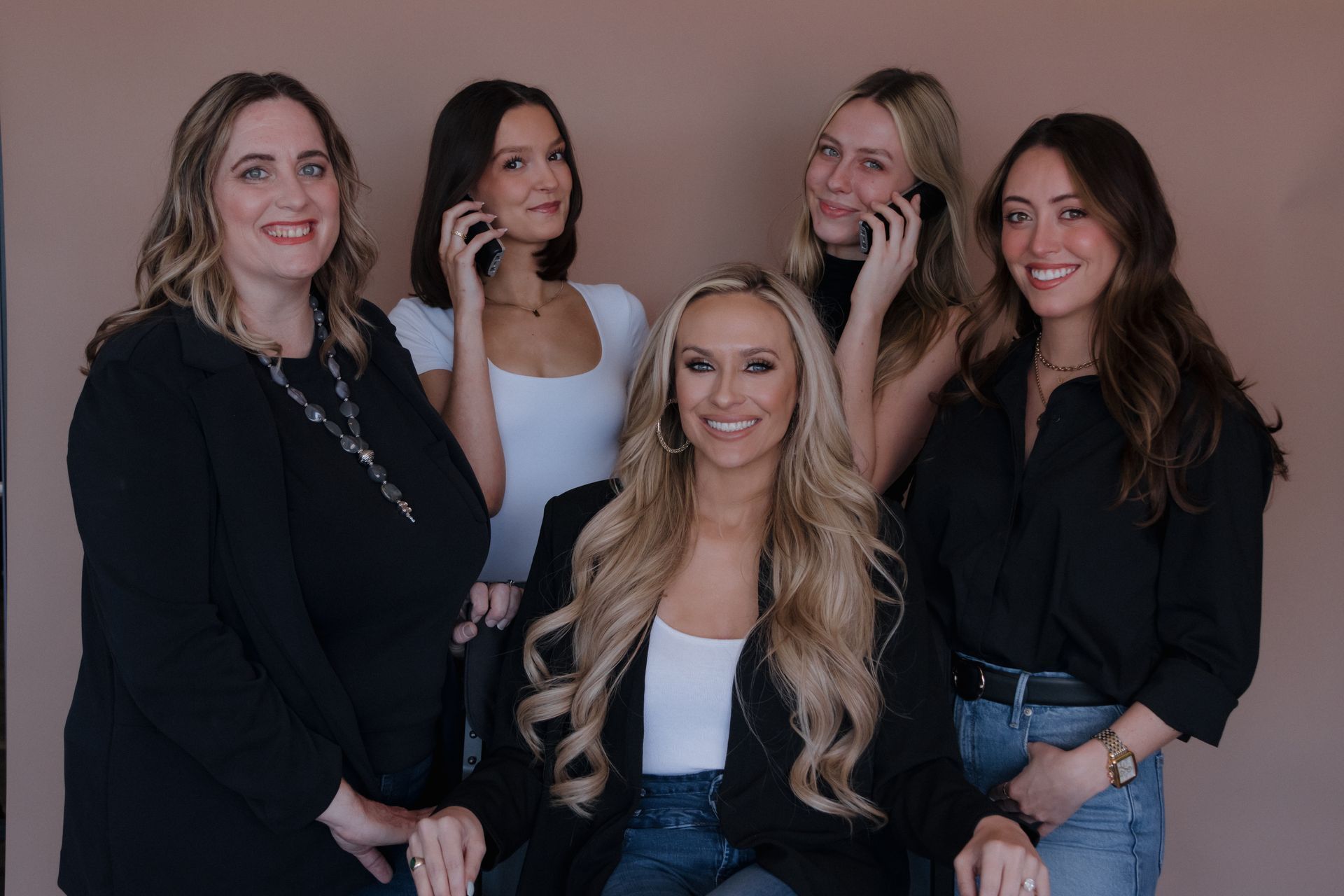 A group of women are posing for a picture while talking on their cell phones.