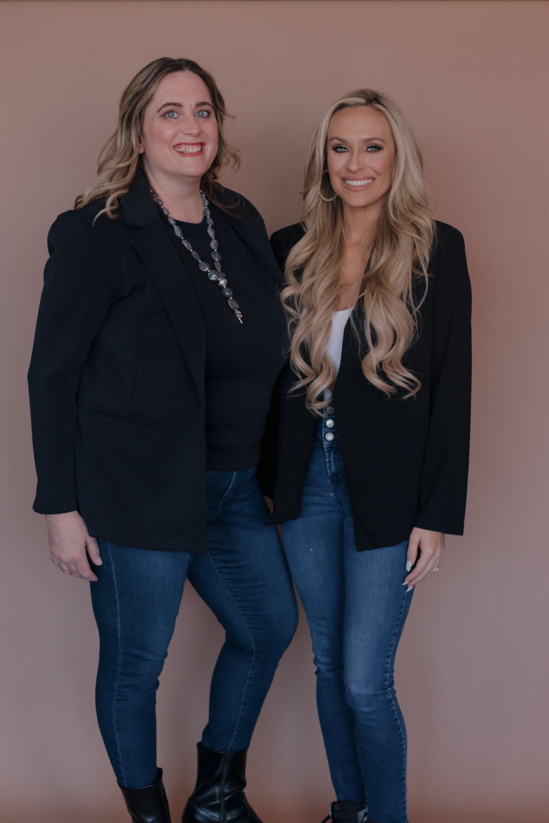 Two women are standing next to each other wearing black jackets and jeans.