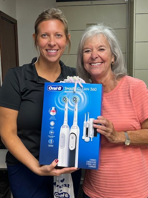Two smiling women hold an Oral-B SmartClean 3000 toothbrush box. One wears a black shirt, the other a pink top.