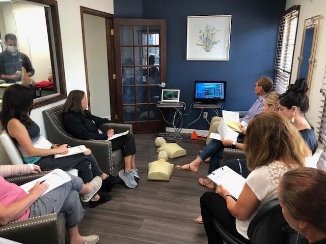 People in a training session, seated in armchairs. CPR training with mannequins and a screen.