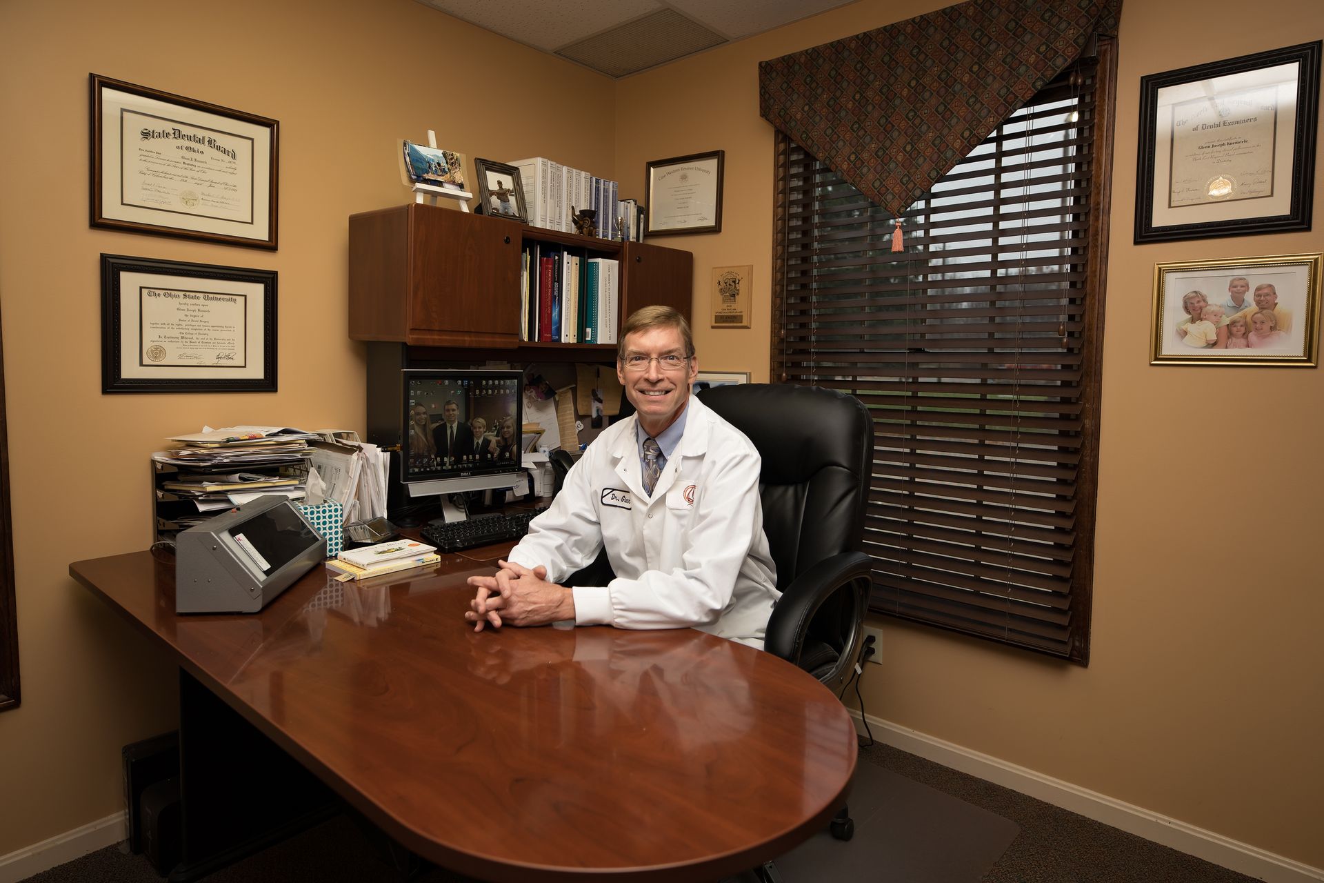 Dentist pointing at a monitor, showing a dental image to a smiling patient in a dentist's office.