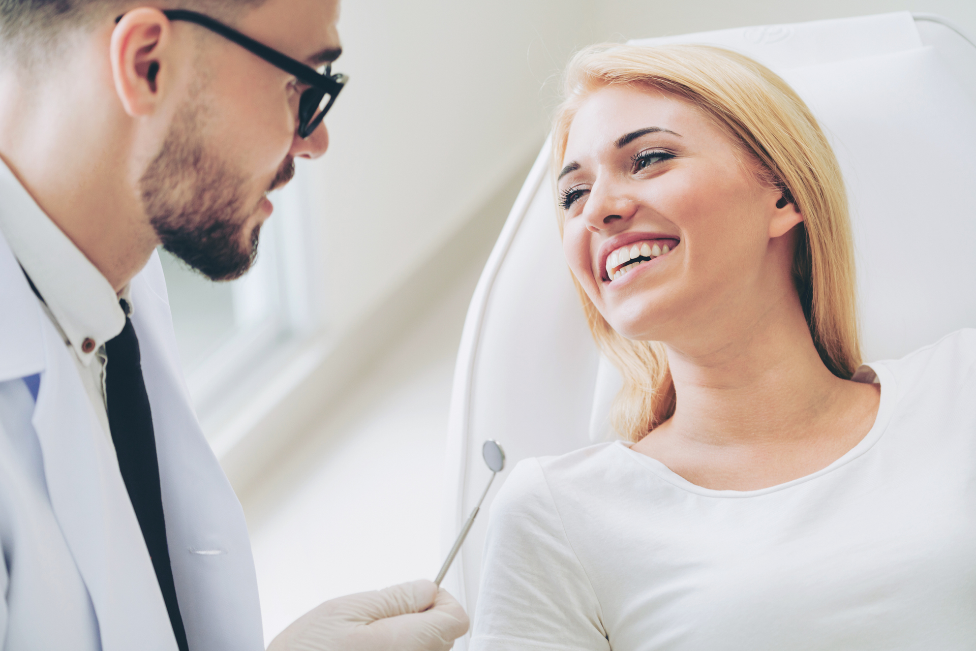 Smiling woman patient at dental checkup with dentist holding mirror for teeth cleaning exam.