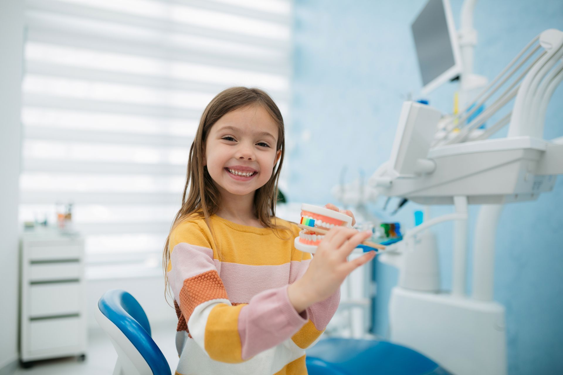 Young person smiling, demonstrating teeth brushing with a model in a dental office.