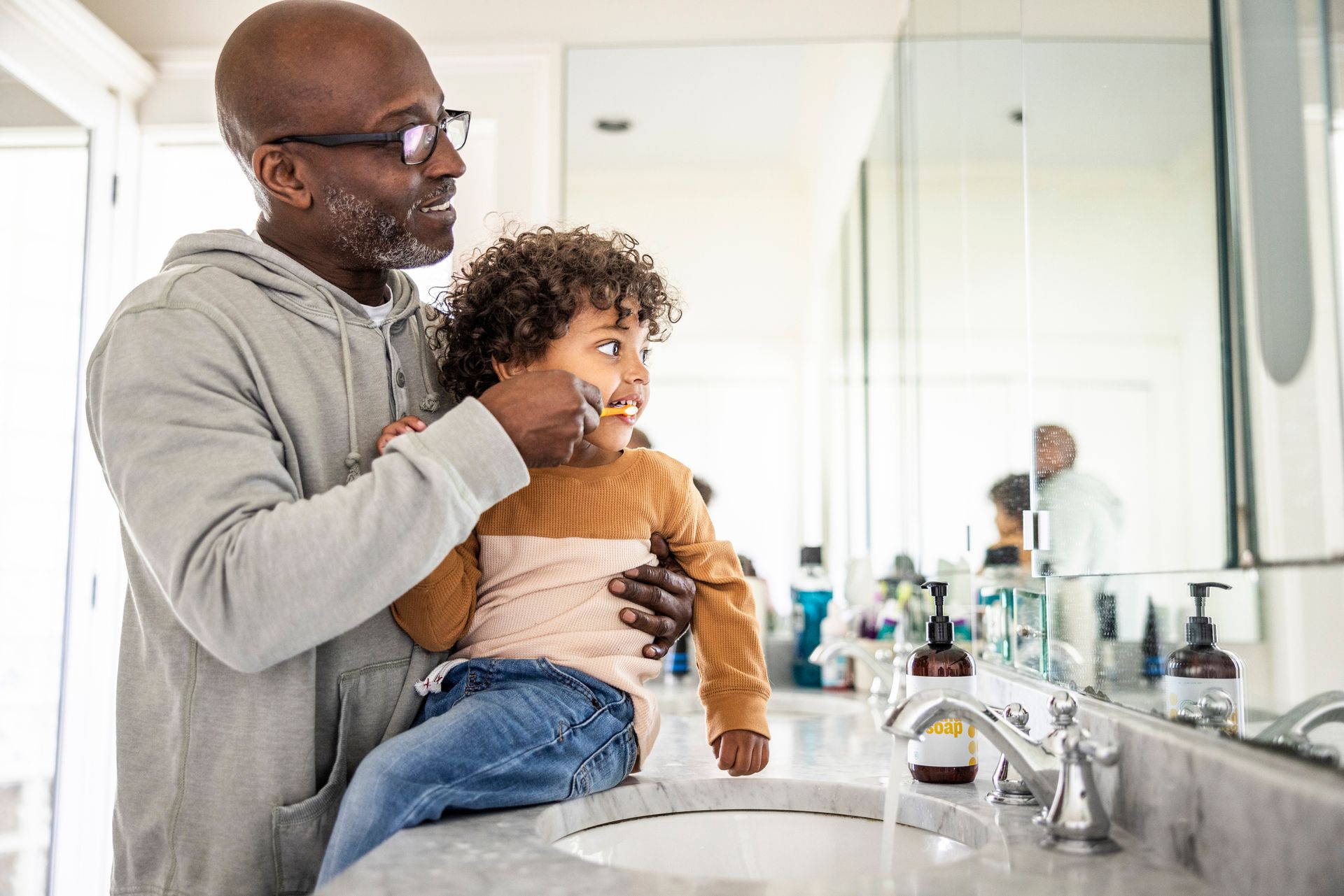 Man holding child, pretending to shave in a bathroom with a mirror.