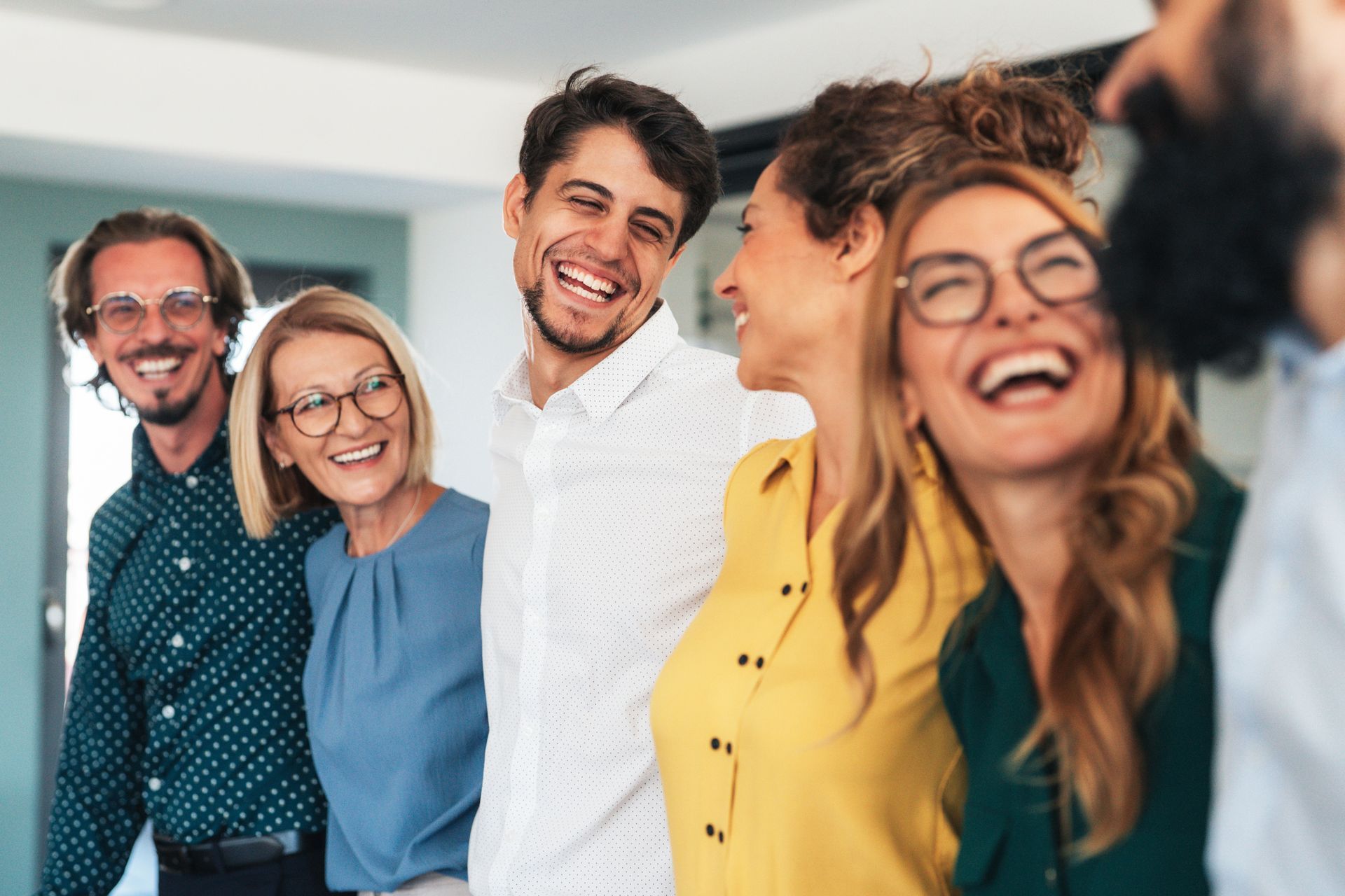 Smiling group of people in an office setting, interacting and laughing.