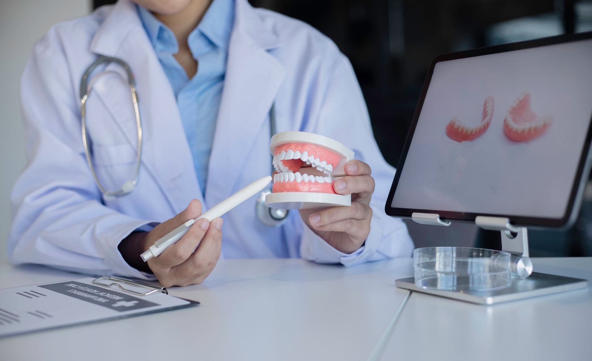 Dentist pointing to model teeth, showing teeth anatomy to patient on tablet.