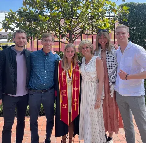 Three people wearing matching race shirts, smiling, pose outside, sunny day.