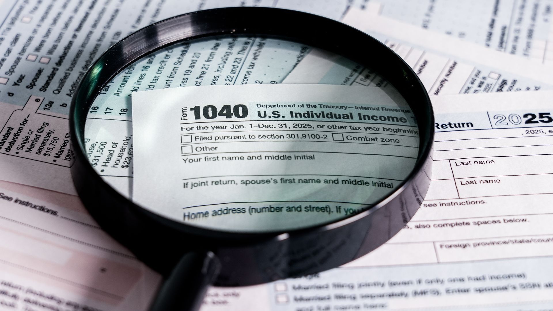 Magnifying glass over IRS 1040 tax form and documents on desk.