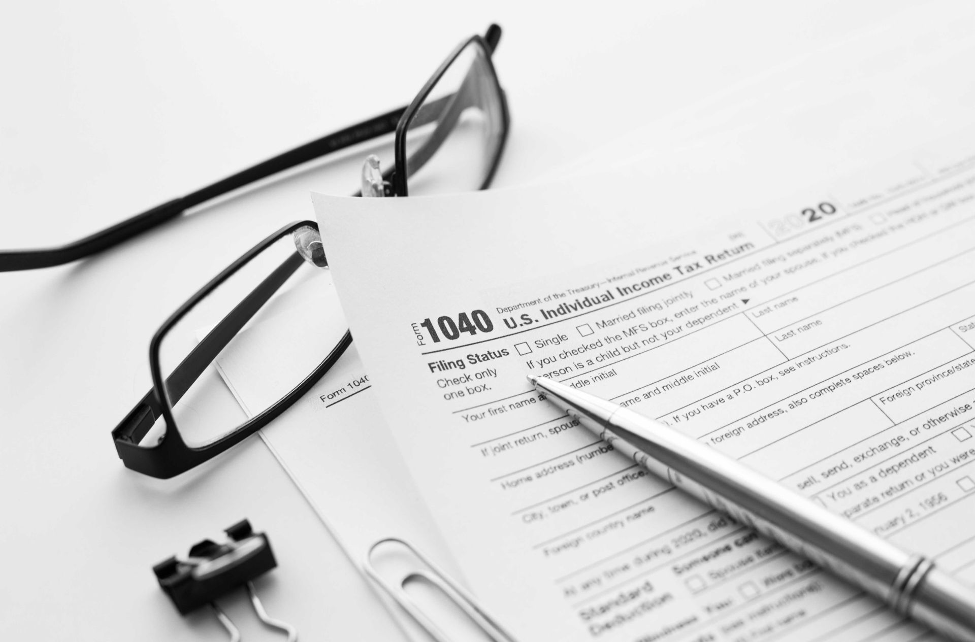 Close-up of tax form 1040 with pencil, eyeglasses, and calculator on top.