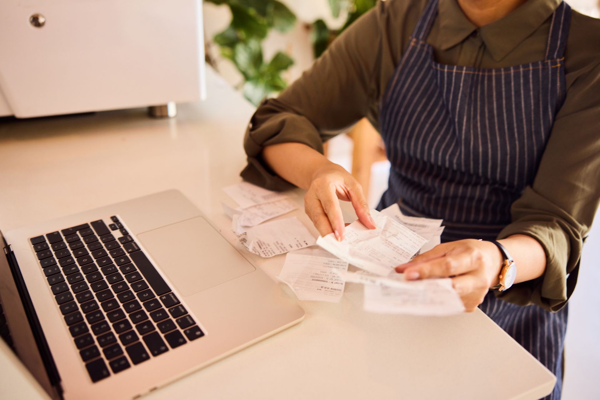 Business owner sorting receipts with a laptop on the desk, in need of business accounting services.