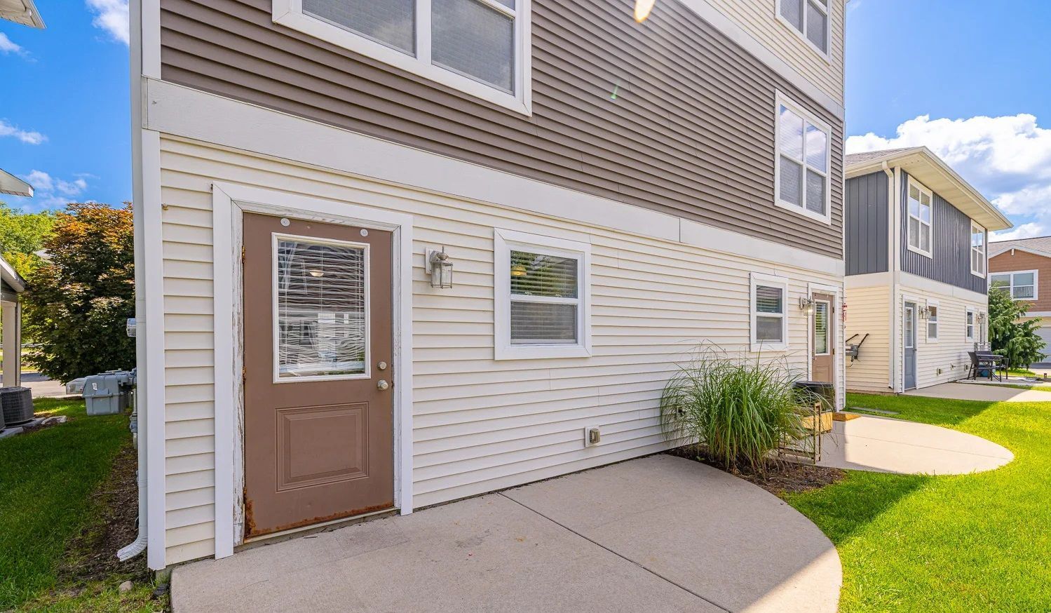 A house with a brown door and a concrete walkway leading to it.