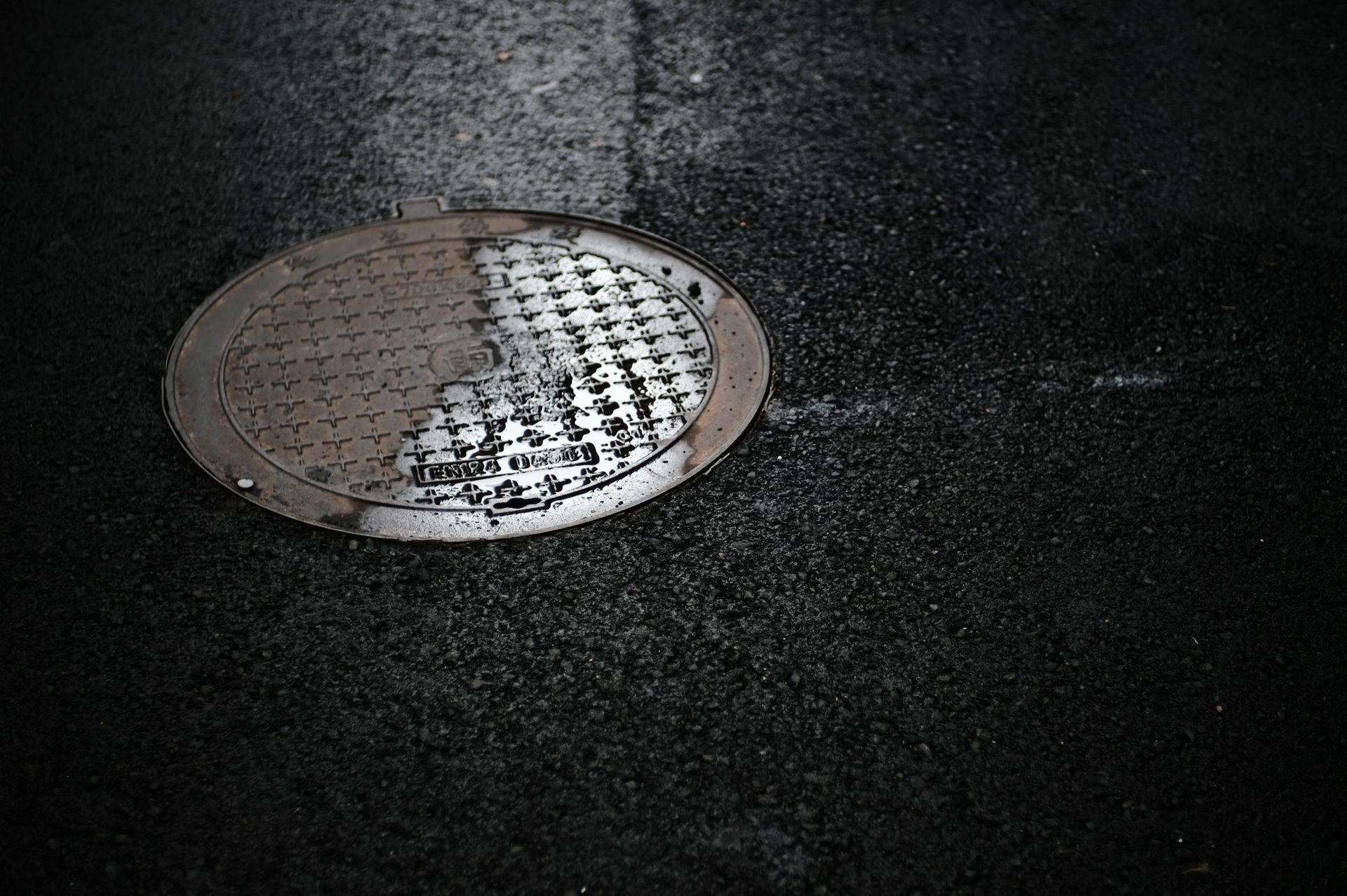 A circular, textured metal manhole cover set into a dark asphalt road surface.