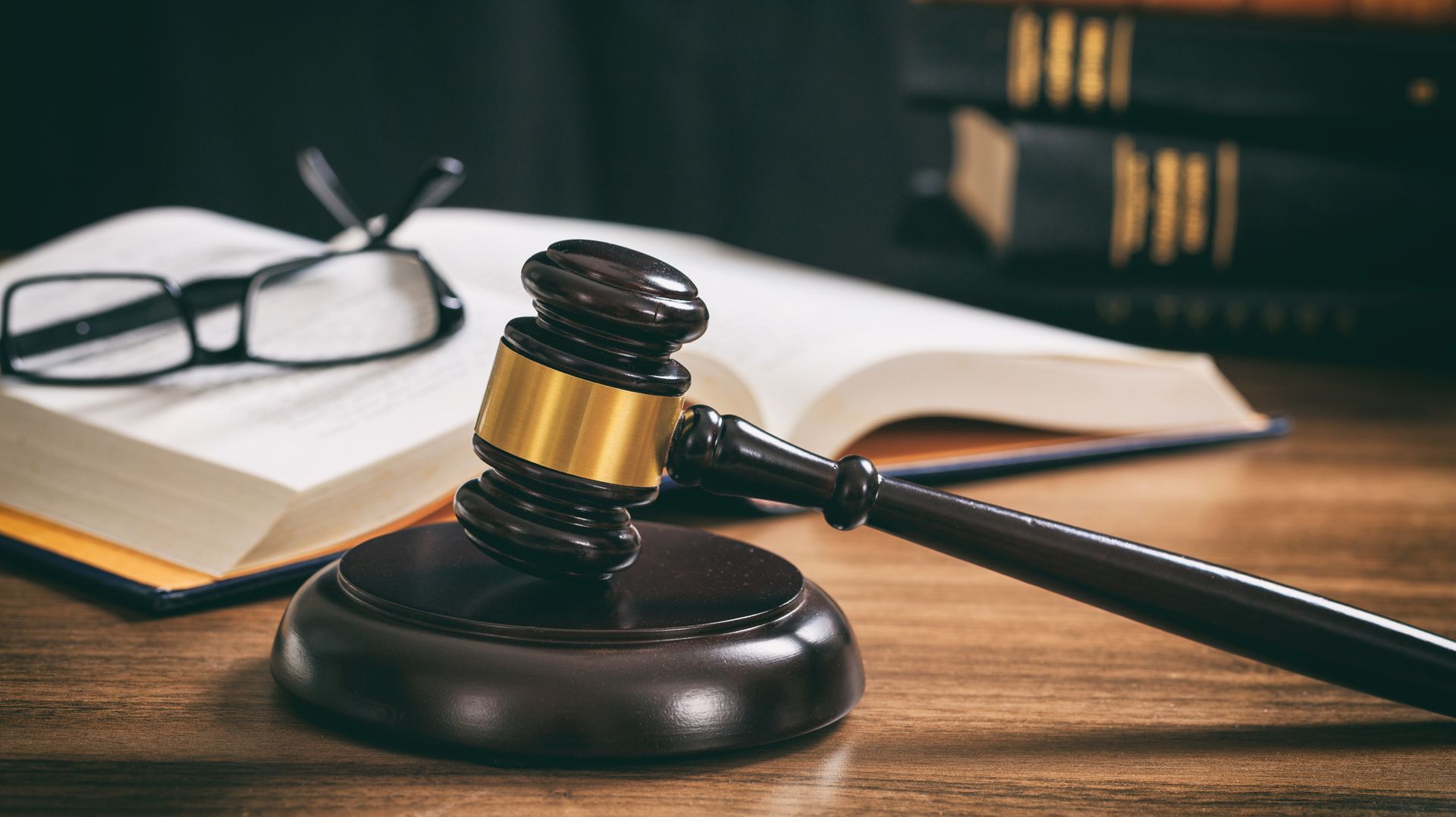Wooden judge gavel with gold band on sound block beside open law book in courtroom.