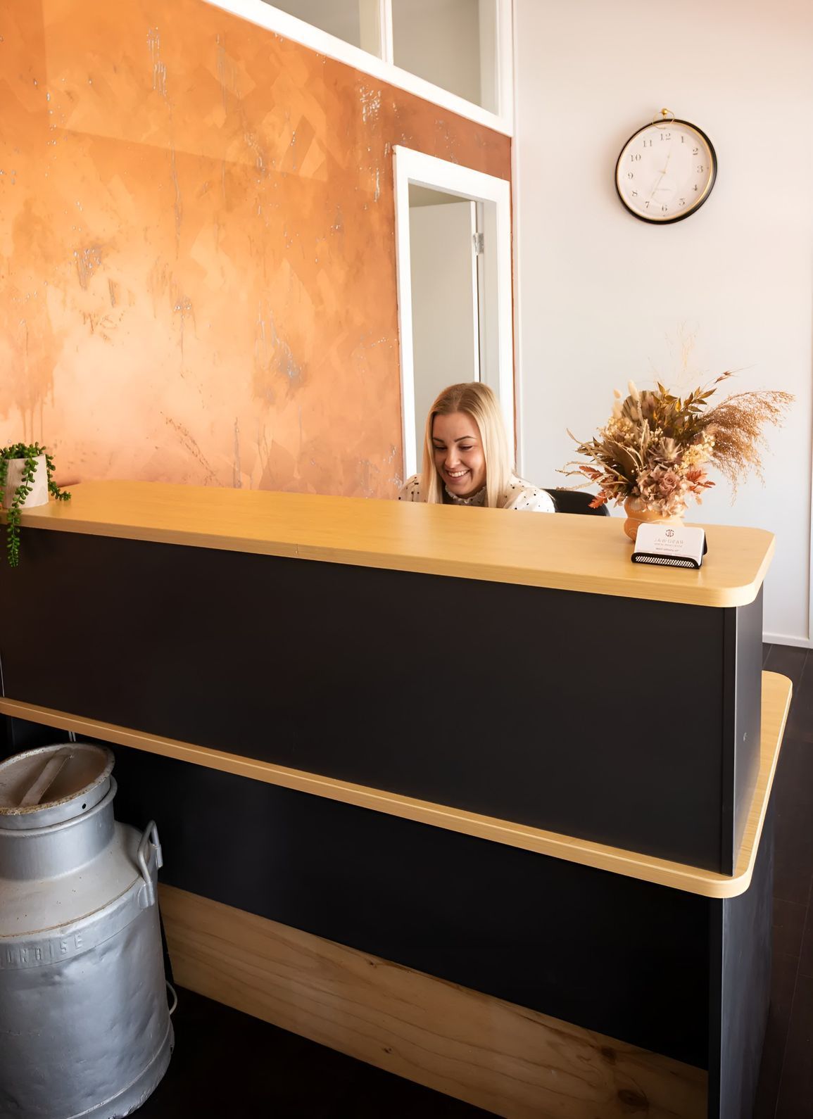 A Woman is Sitting at a Reception Desk in a Room With a Clock on the Wall — Jaw Gear Dental Prosthetics in Bowral, NSW