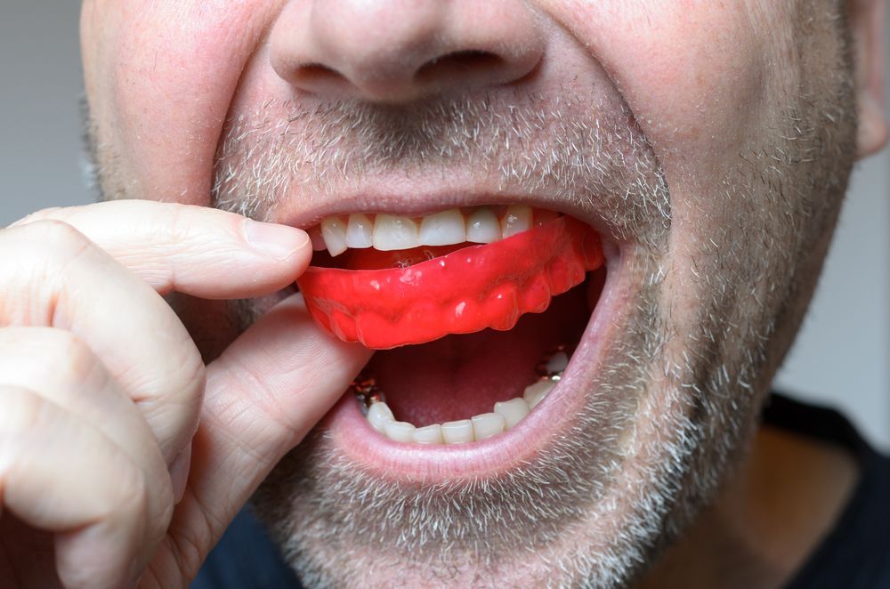 A Man is Putting a Red Mouth Guard in His Mouth — Jaw Gear Dental Prosthetics in Mittagong, NSW
