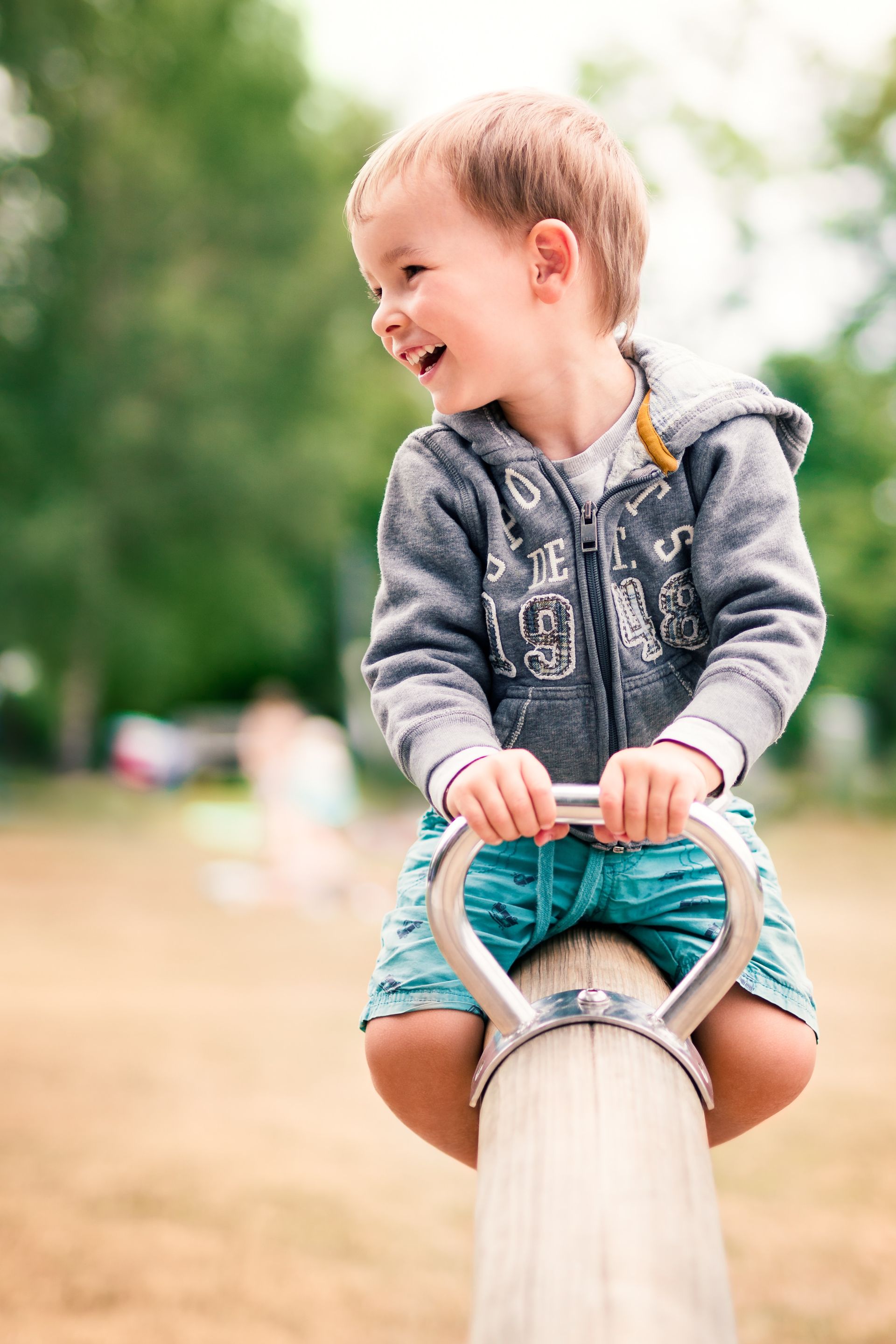 A young boy is sitting on a seesaw in a park.
